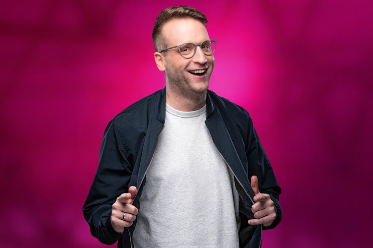 Benny Stark zeigt mit zwei Fingern auf das Publikum vor rosanem Hintergrund