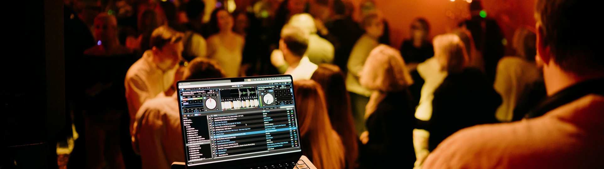 DJ Pult auf einer Bühne vor tanzenden Menschen