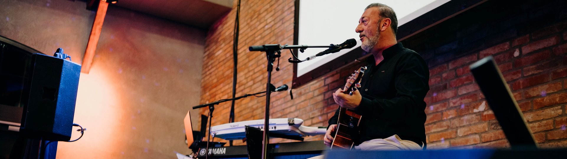 Mann mit Gitarre am Mikrofon auf einer Bühne