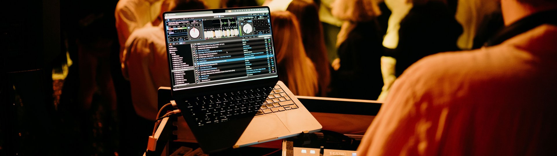 DJ Pult auf einer Bühne vor tanzenden Menschen