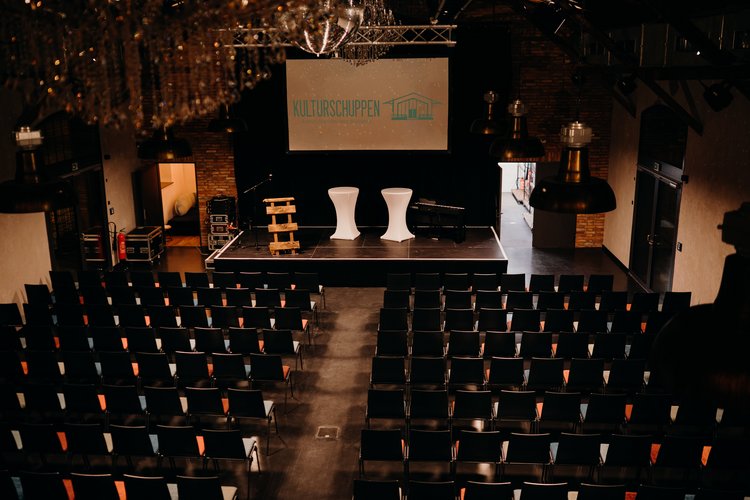 Veranstaltungsbestuhlung von oben fotografiert, Leinwand mit Schriftzug "Kulturschuppen" im Hintergrund