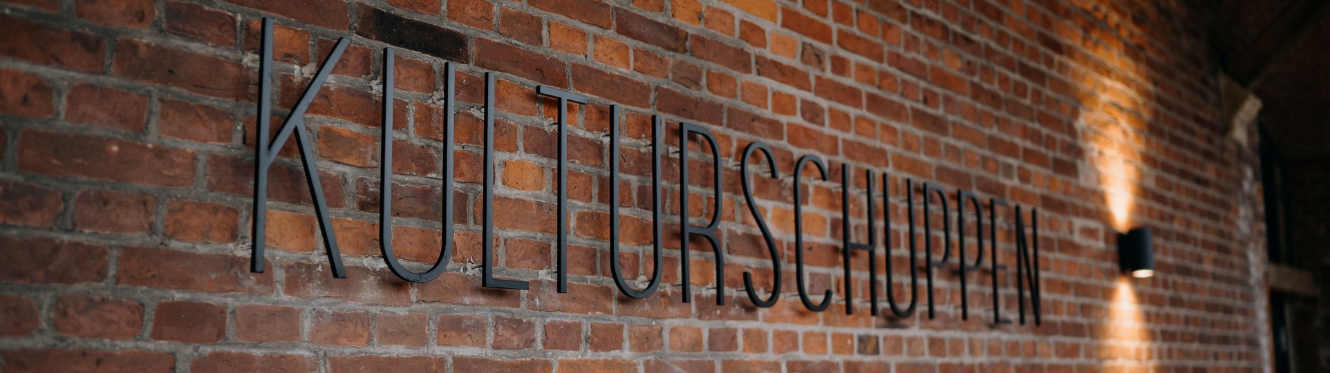 Metall Schriftzug "Kulturschuppen" an einer Backsteinmauer