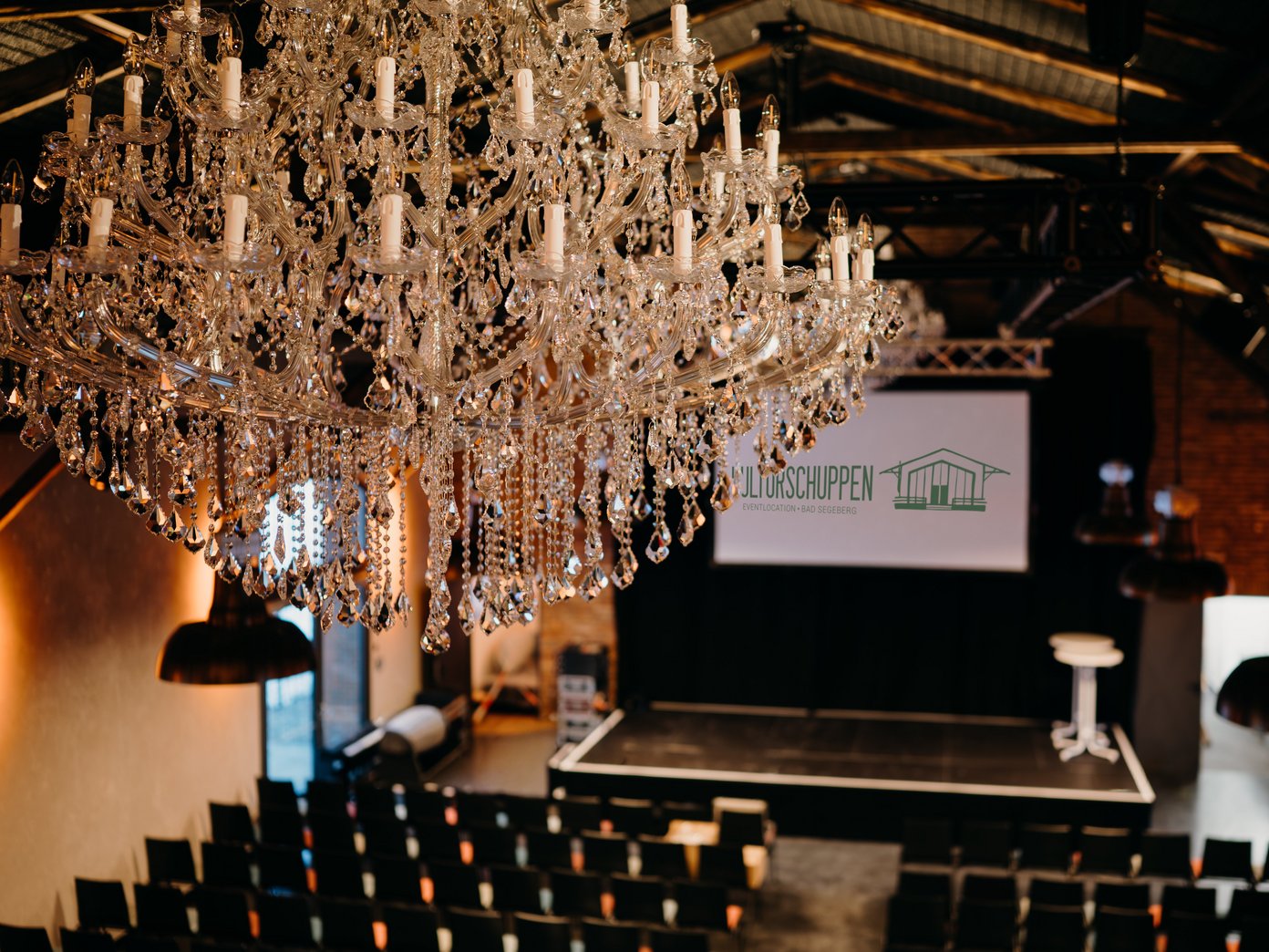 Kronleuchter vor Reihenbestuhlung, Leinwand mit Schriftzug "Kulturschuppen"