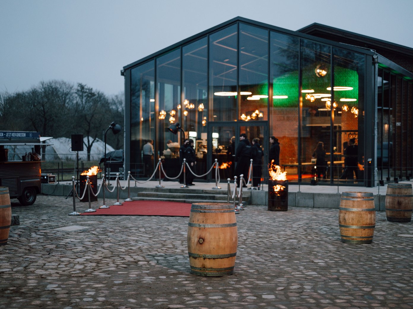 Weinfässer auf Kopfsteinpflaster vor einem Wintergarten mit rotem Teppich