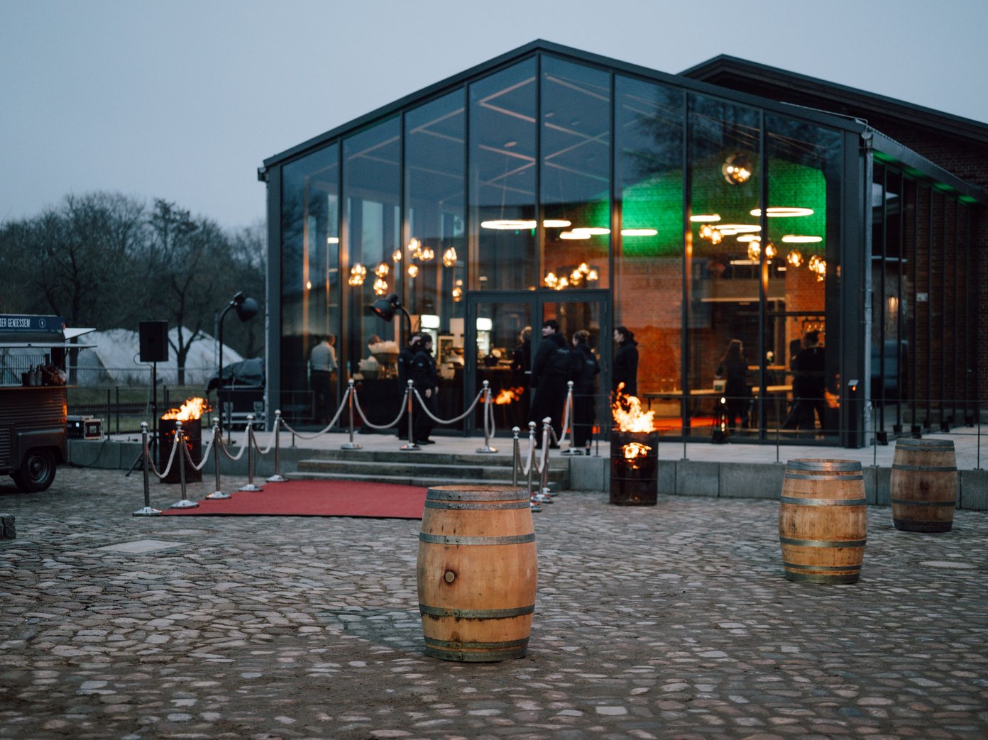 Weinfässer auf Kopfsteinpflaster vor einem Wintergarten mit rotem Teppich