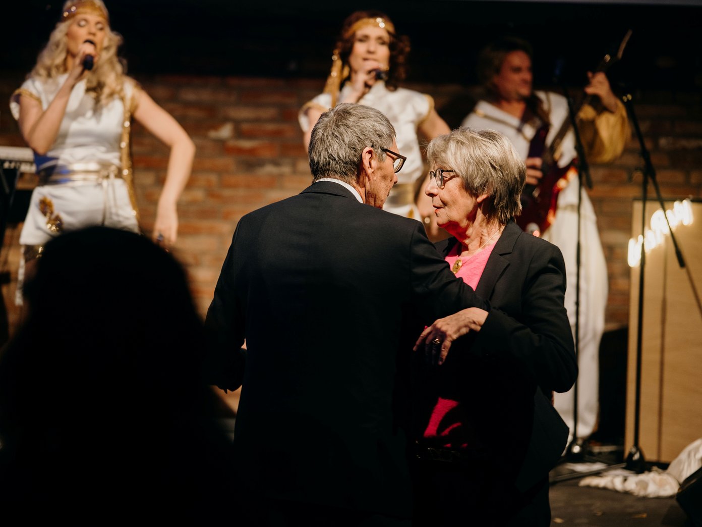 Altes Paar beim Paartanz, zwei Sängerinnen auf der Bühne dahinter