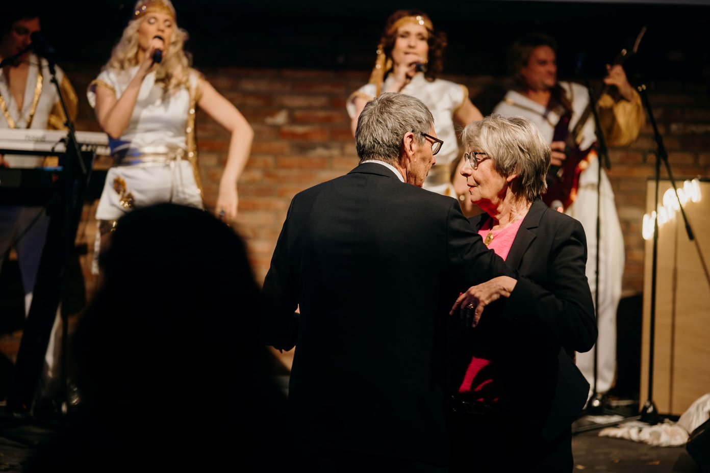 Altes Paar beim Paartanz, zwei Sängerinnen auf der Bühne dahinter