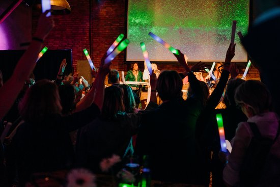Viele Menschen mit bunten Lichtstäben vor einer Bühne
