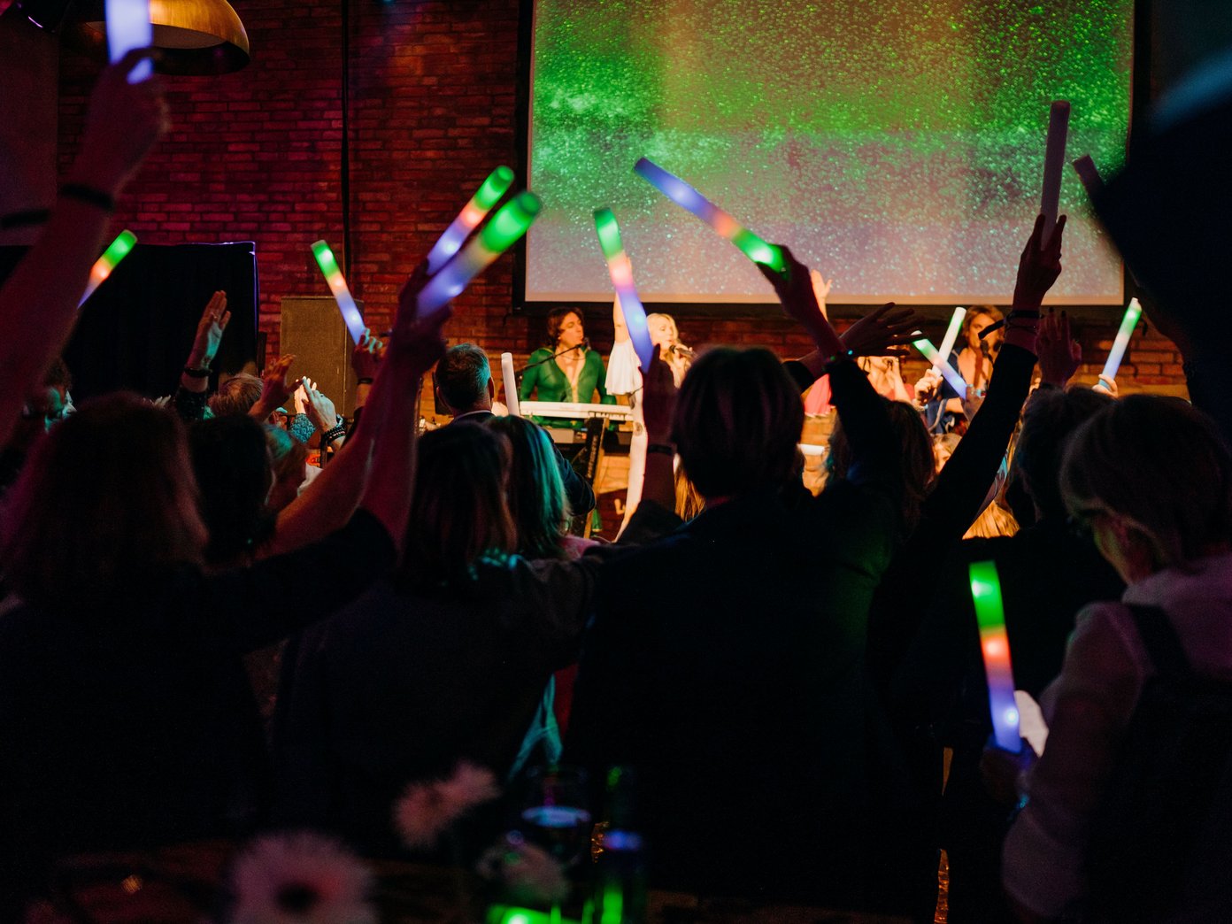 Viele Menschen mit bunten Lichtstäben vor einer Bühne